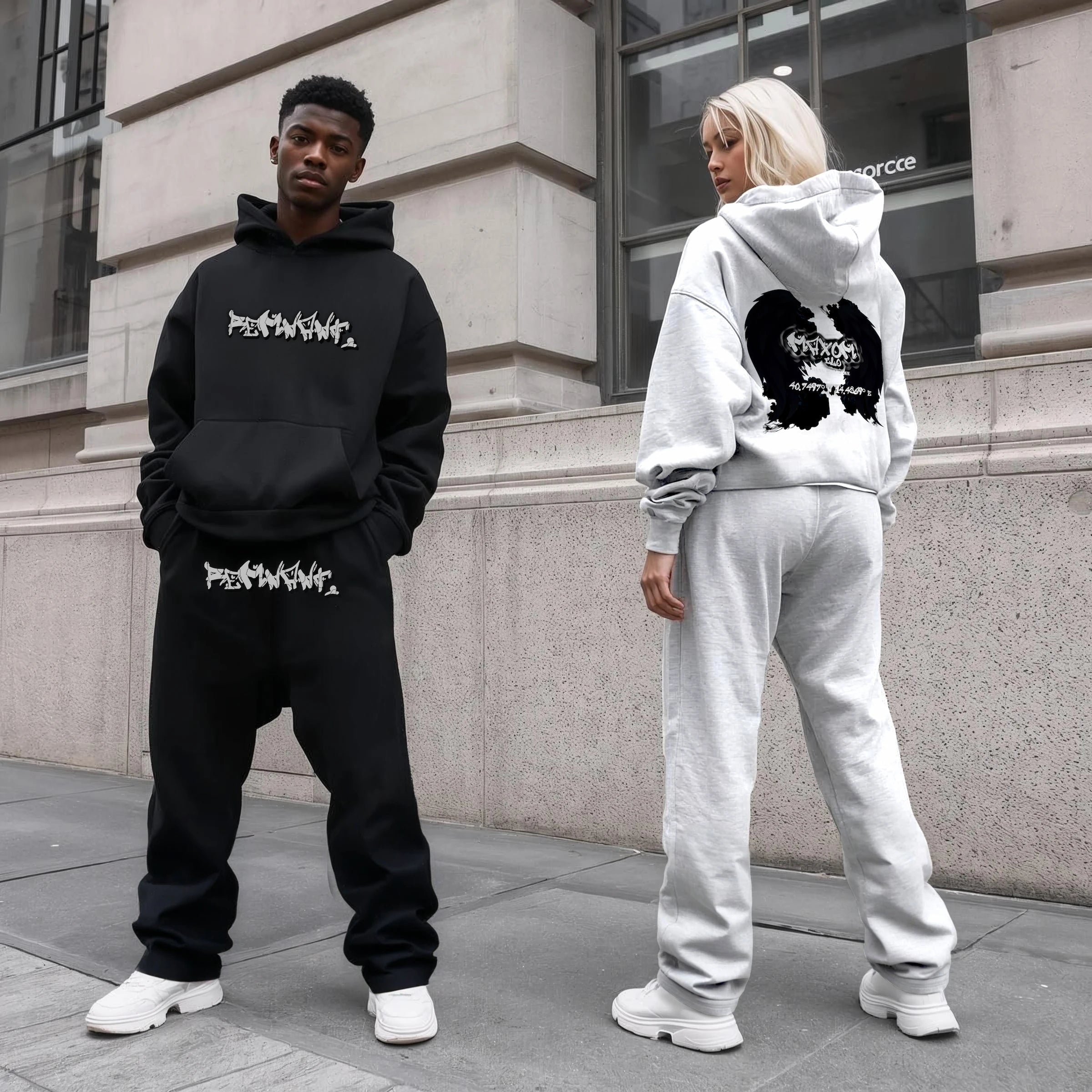 Man in REMNANT. black oversized hoodie and baggy graffiti sweatpants next to woman in grey zip hoodie with angel wings backprint – heavyweight streetwear tracksuits from the Fall 2025 urban fashion drop.